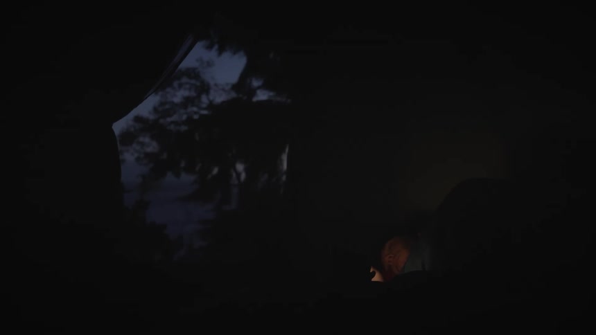 A man sleeping in a tent is using his smartphone