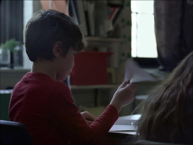 A clip of a boy in a classroom playing with a paper plane