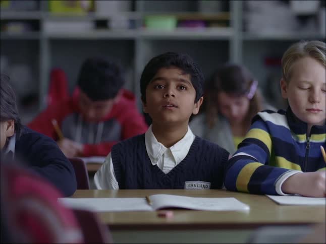 An indian kid sitting next to a white kid in a classroom