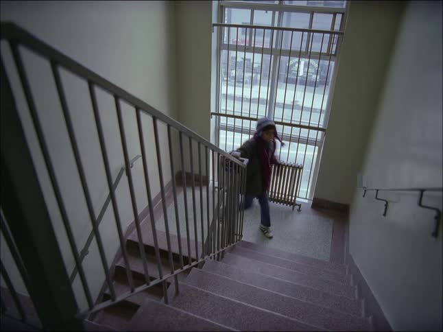 A young boy in warm clothes is running up stairs with a handrail