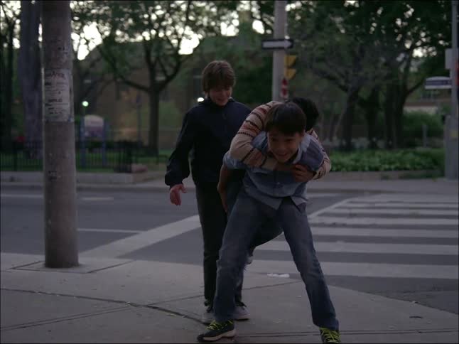 Children playing stacking on top of each other on the sidewalk next to the street