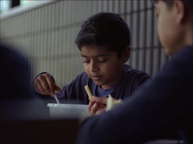 Two children in blue uniforms are eating while sitting at a table