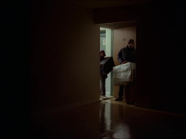 A father and his son enter a dark room through a door and have bags in their hands