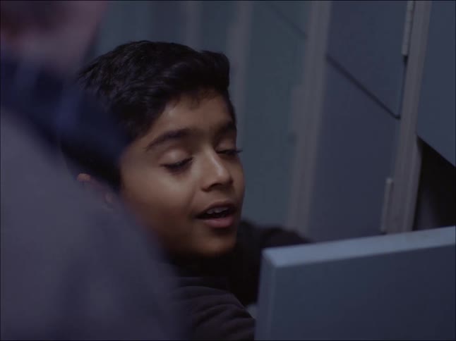 Portrait of a young boy crouched down at a school locker talking to a person beside him