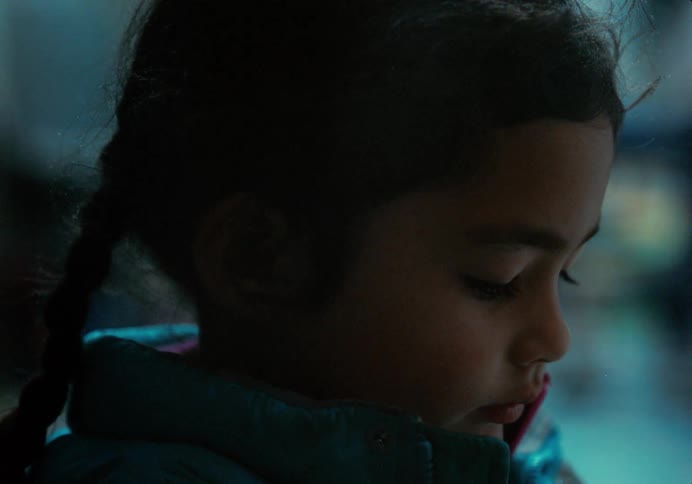 A little girl with braids in her hair is looking down
