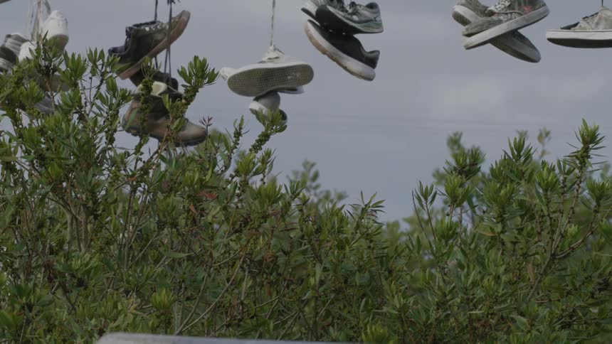 A person riding a skateboard with several sneakers hanging from the wire