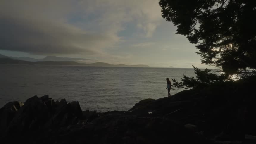 A person on the rocky shore of the sea at sunset
