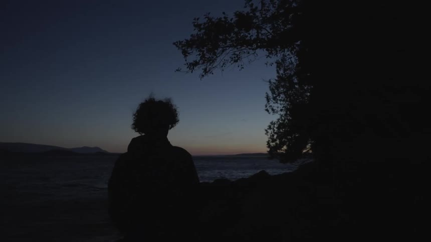 Man facing the sea with his back to the viewer under a dark dawn sky