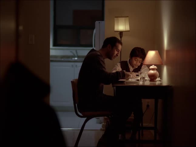 Father and son eating food indoor while sitting at the table at night