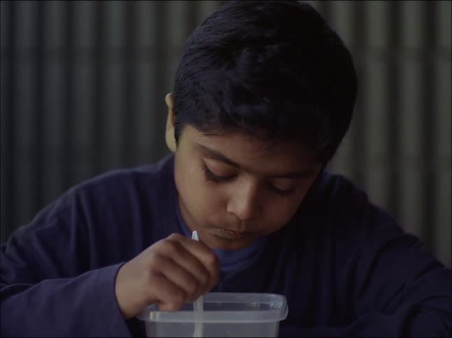 A young little boy is sitting and eating using a spoon