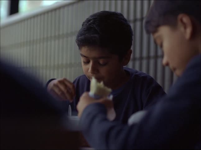 Two boys in blue uniforms are sitting at the table eating