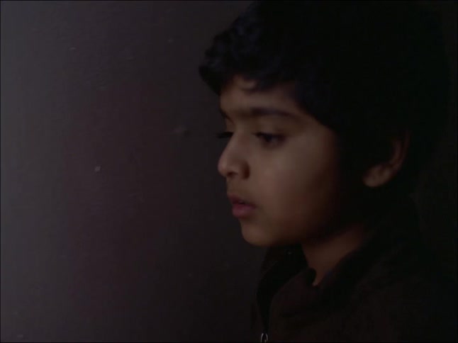 A little boy walks through a dark door and looks straight ahead with his face illuminated by natural light