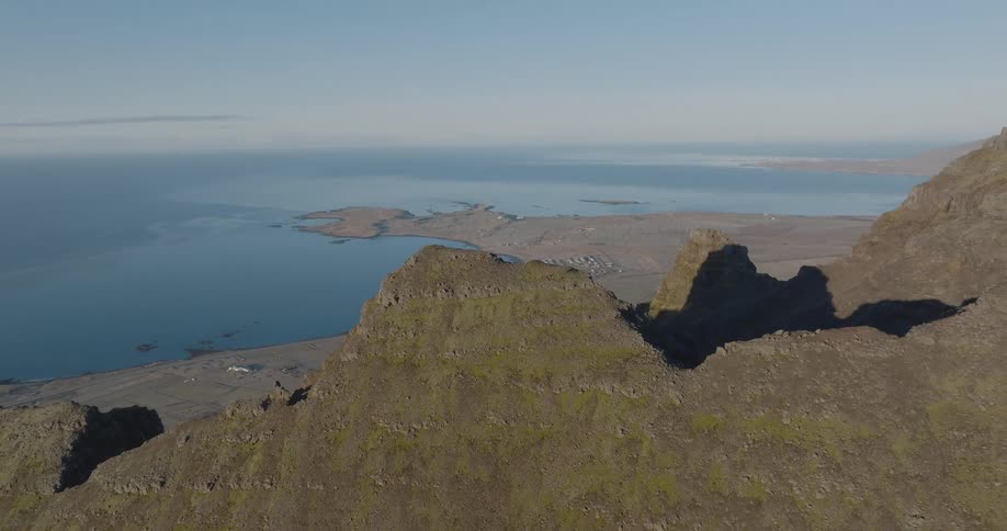 The peak of a stone mountain and beyond is a coast with the ocean