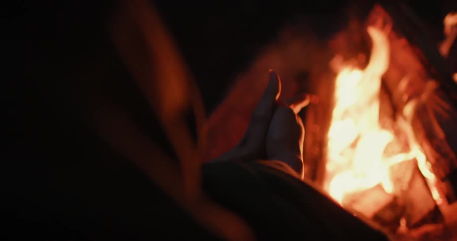 A person is warming their hands near a campfire