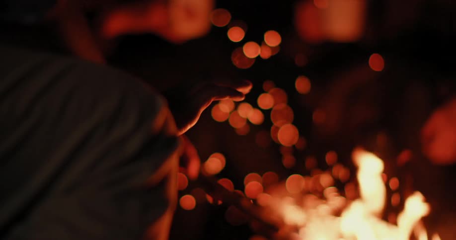 People sitting by a campfire at night and holding a stick over the fire