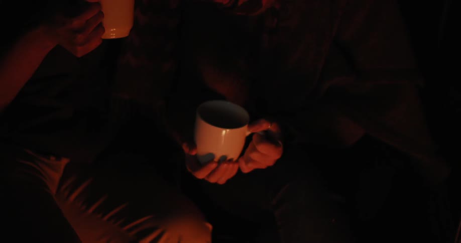Two people holding mugs sit beside fire