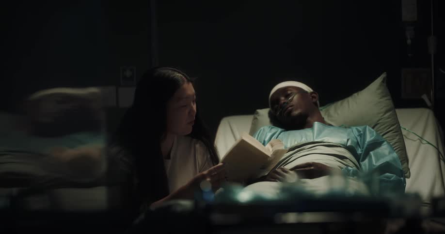 Woman reads to man laying in hospital bed