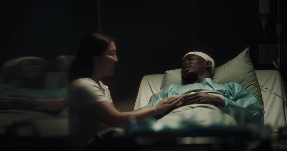 Woman leans over hospital bed to kiss man smile and laugh