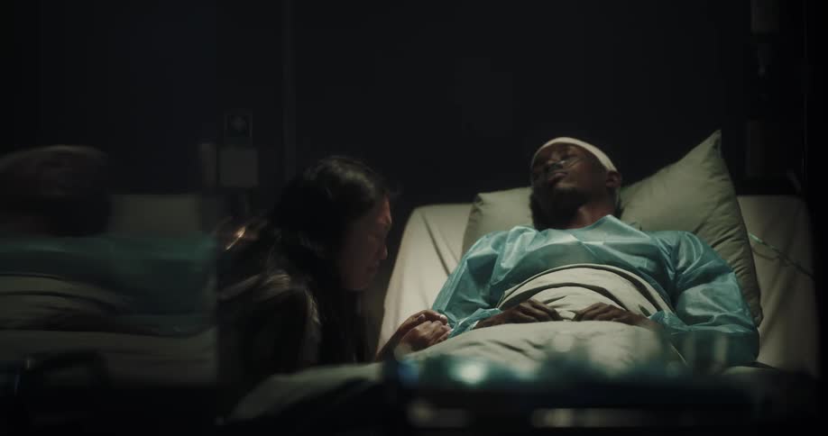 A woman crying by the side of her partner who is lying motionless on a hospital stretcher