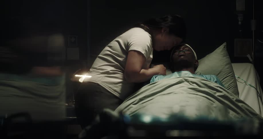 Woman leans over man laying in hospital bed