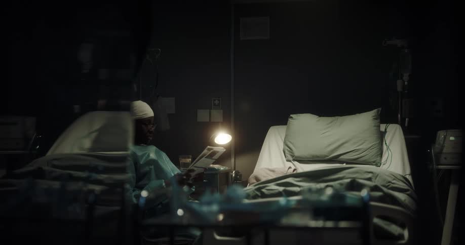 Black man sits in chair in dark hospital room