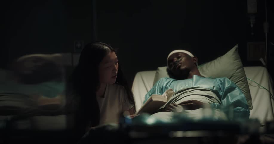 Woman reading a book and looking at her partner lying on a hospital stretcher beside her