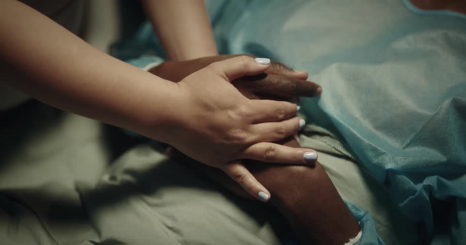 A visitor holds the hands of a patient in the hospital