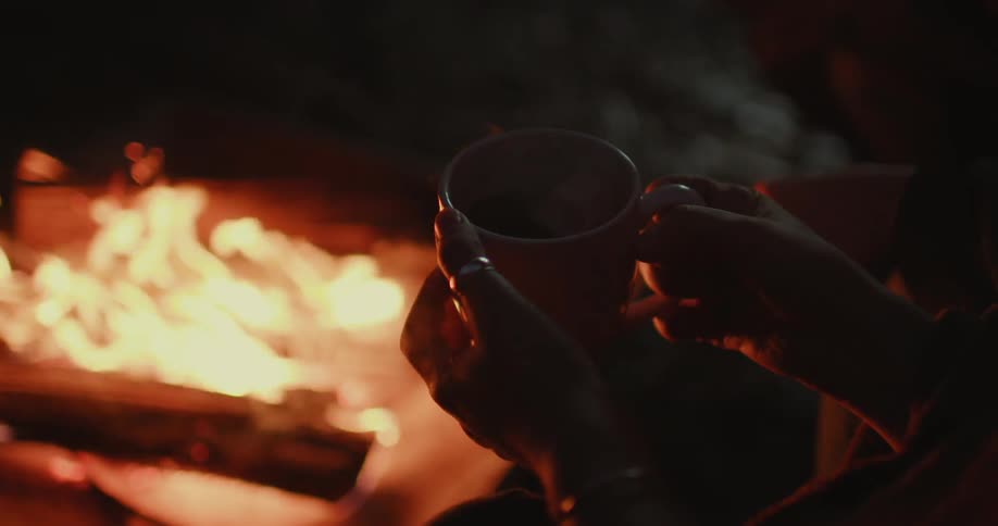 A person is holding a mug near a campfire