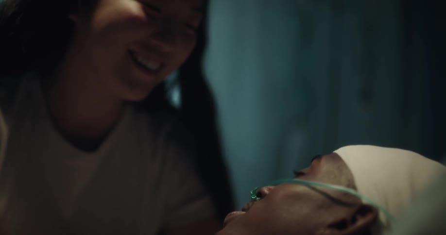 Asian lady smiling and talking with a black man laying on hospital bed with tube in his nose
