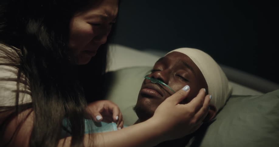 A woman crying and giving a kiss to her partner lying motionless on a hospital stretcher