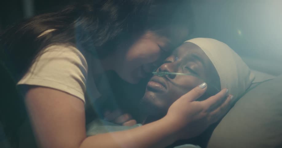 Woman crying and giving a kiss on the face of a man lying in a hospital bed