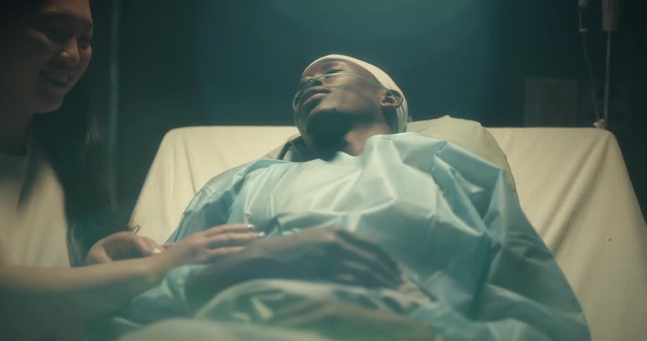 A woman touches and kisses a man wearing a nasal cannula while lying in a hospital bed for support