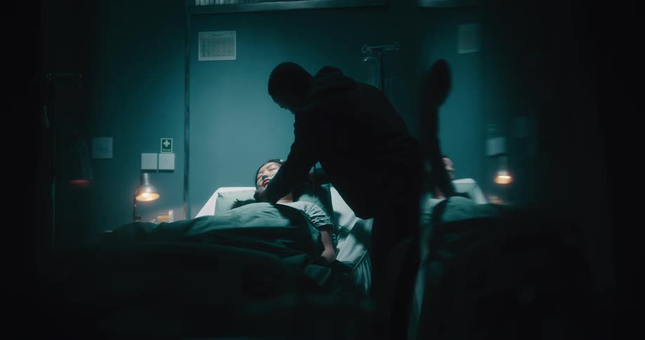 Sick asian lady sleeping on the hospital bed being checked on by a black man