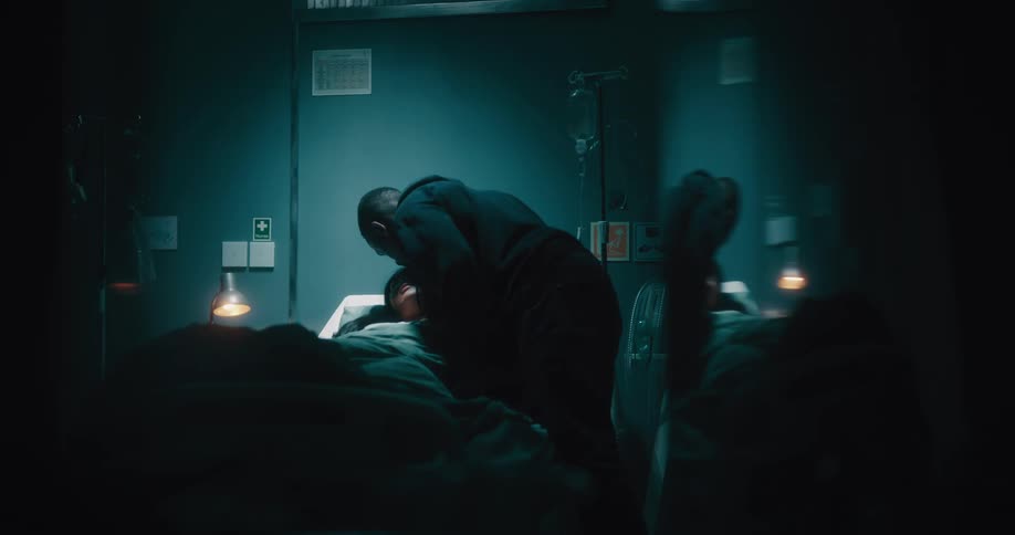 A man kissing his wifes forehead while she is unconscious and lying on a hospital stretcher