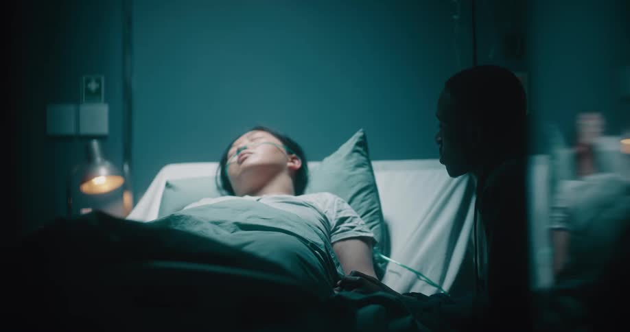 Sad man by the side of his wife who is sleeping on a hospital stretcher