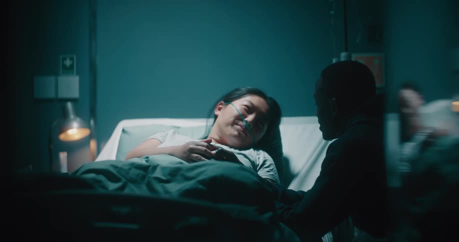 Sick lady on the hospital bed and a man seated close by talking while holding hands