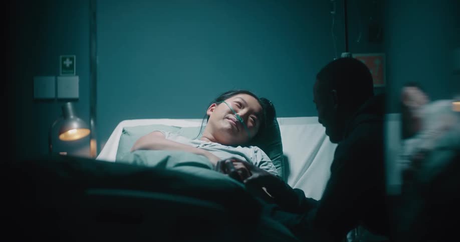 Smiling man having a conversation with his wife who is lying in the hospital bed