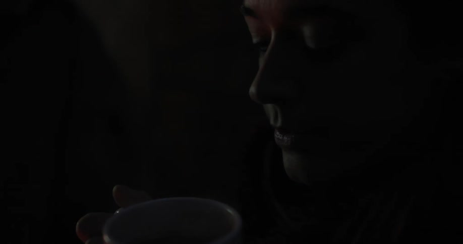 A woman holding and looking a steaming mug outside at night