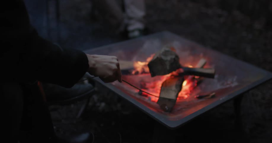 People putting sticks in a small campfire at night