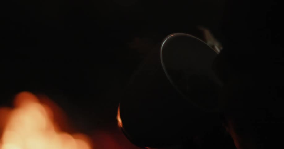A person sitting near a fire drinks from a mug