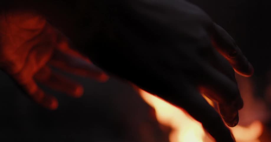 A person is warming their hands on a fire at night