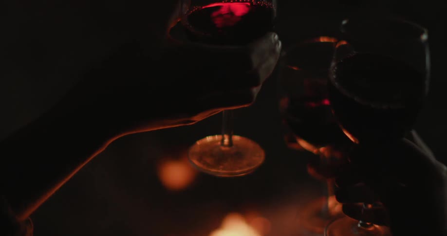 Three people doing cheers with their wine glasses by a small campfire at night