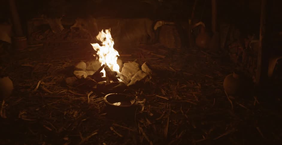 A small campfire burning at night near a pot of water