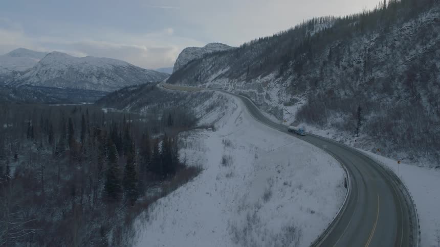 A semi truck drives down a winding mountain road during the winter