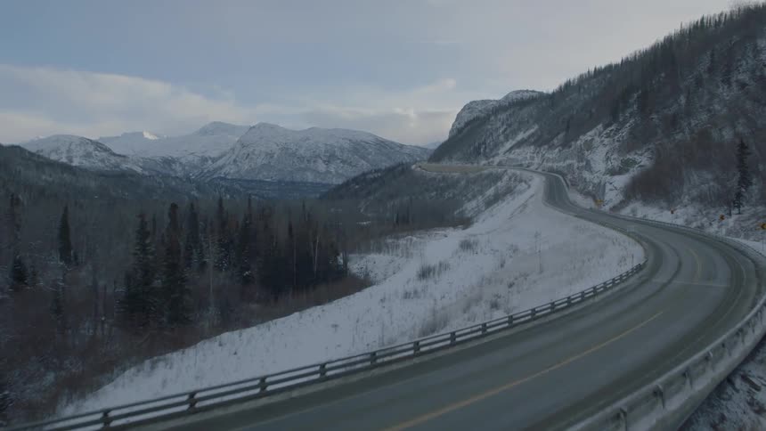 Ascending over a frozen river bridge to reveal a winding mountain highway