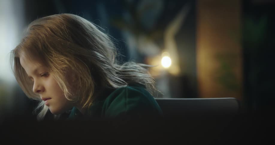 Blonde girl with a green hoodie sits at desk writing in a notebook by looking at the laptop