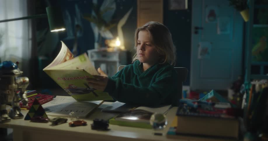 A blonde girl wearing a green hoodie flips through a book and writes in a notebook