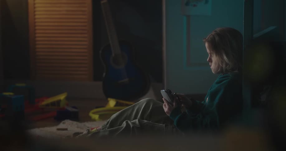 Blonde girl wearing a green hoodie sits on the floor holding a small drone
