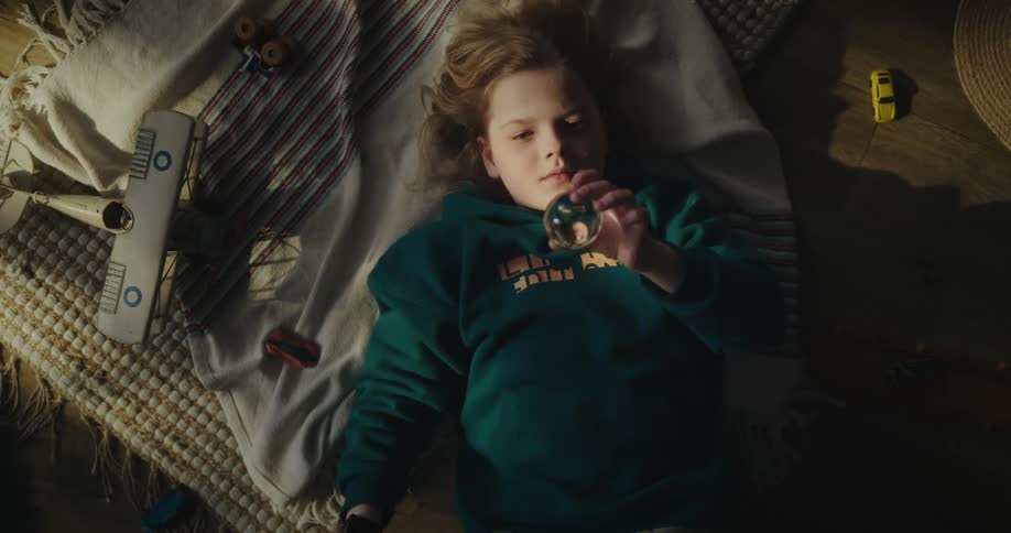 Portrait of a girl lying on the floor playing with and observing a small crystal ball