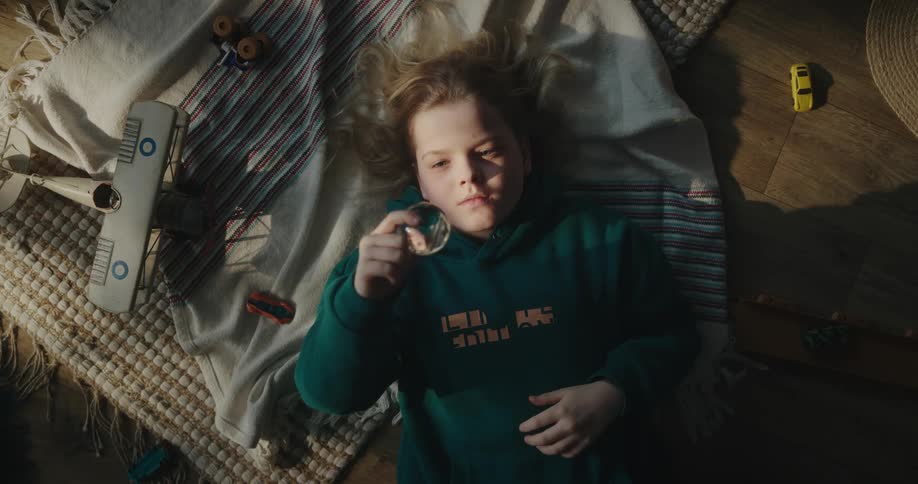 Blonde girl with a green hoodie lies on bed looking at a transparent ball